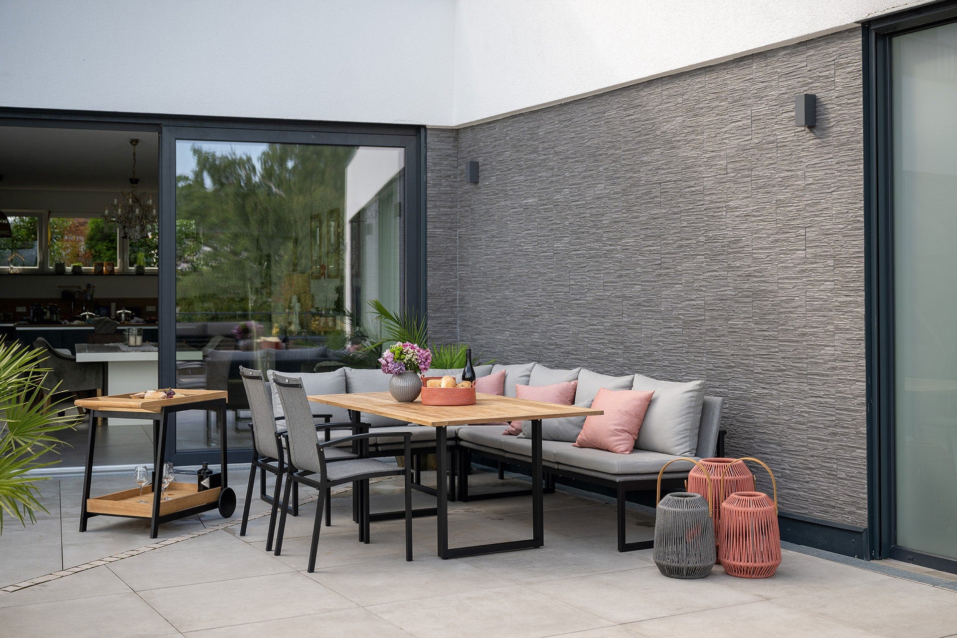 Moderne Terrassenecke mit Eckbank, Esstisch aus Holz, Polsterkissen in Rosa und grauen Outdoor-Laternen von BOKORA.