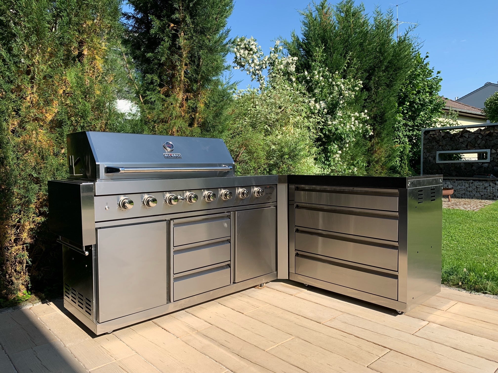 Modulare Outdoorküche aus Edelstahl mit großem Gasgrill und Stauraumelementen von ALLGRILL auf Terrasse im Garten.