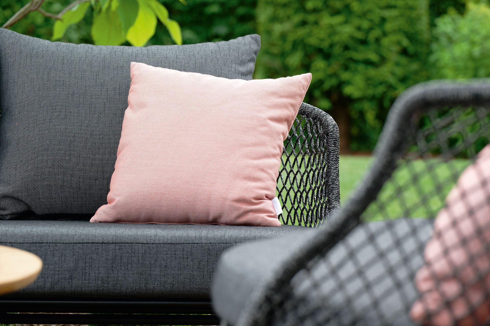 Graue, moderne Gartenmöbel mit hellroten Kissen, im Hintergrund Garten.