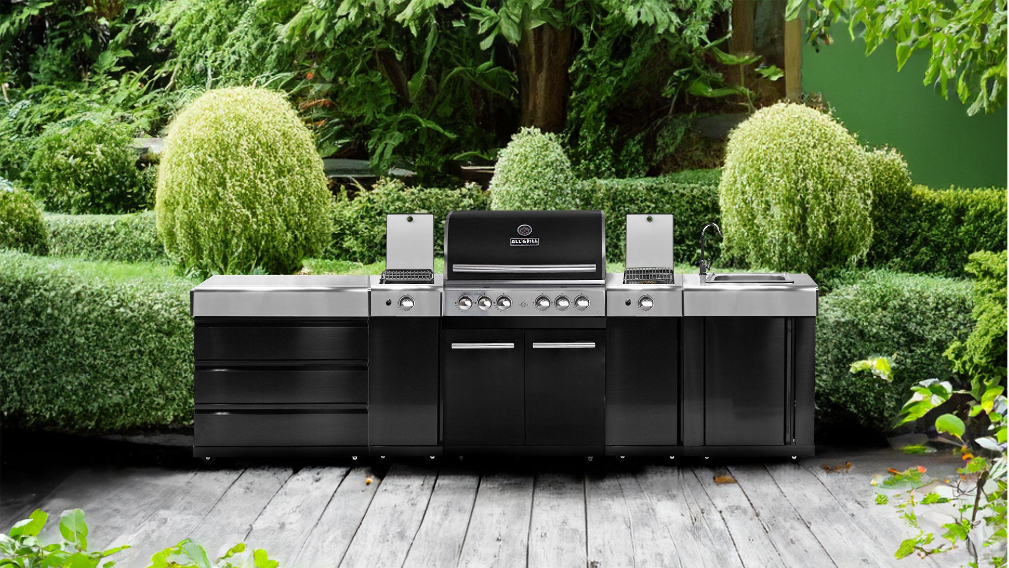 Moderne Outdoor-Küche mit Gasgrill, Seitenbrennern, Spüle und Stauraum von ALLGRILL auf Holzterrasse vor grünem Garten.